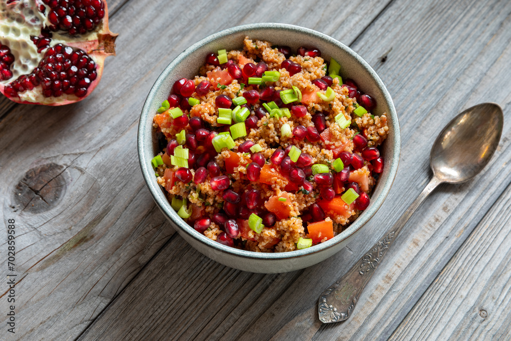 Homemade kisir - spicy Turkish bulgur wheat salad in a bowl, half a pomegranate, and a spoon, next to it. Homemade kisir - spicy Turkish bulgur wheat salad in a bowl, half a pomegranate, and a spoon, next to it.