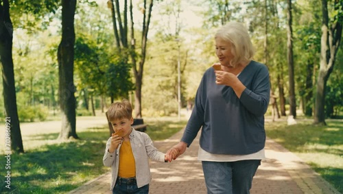 Active granny and cute grandson eating ice cream, walking in park together photo