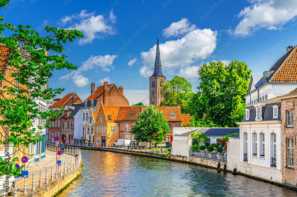 Obraz premium Sint Annarei water canal of Reie river, old buildings on embankment in Brugge old town, Bruges city historical centre, Saint Anna Church tower spire, West Flanders province, Flemish Region, Belgium