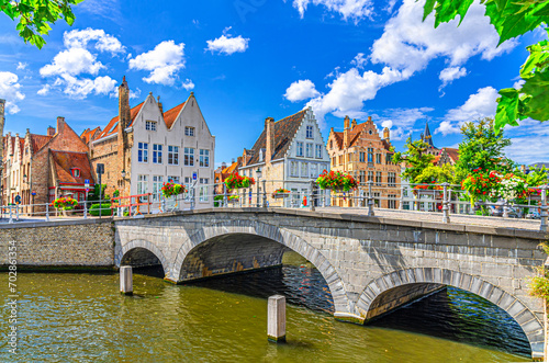 Carmersbrug Carmelite Bridge across Langerei canal, stone arch bridge with flowers on fence, old houses on embankment, Brugge old town district, Bruges city historical center, West Flanders, Belgium