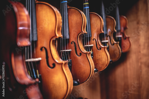 Row of multiple violins hanging on the wall, musician workshop