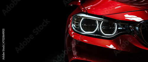 Closeup on headlight of a generic and unbranded red car on a black background © daniy