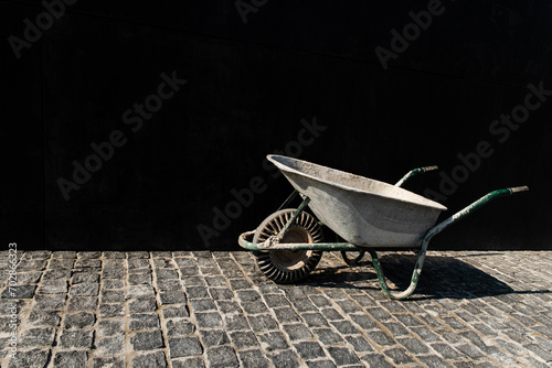Empty wheelbarrow on a brick road and a black background wall at the construction site