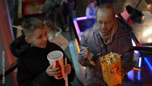 Brother and sister going to the cinema. Girl holds popcorns, boy holds the soda drink.