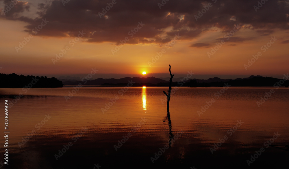 Sunset in winter season at reservoir with the tree trunk, silhouette mountain with dry tree trunk in water at Pom Pee viewpoint is located in Khao Laem National Park, Kanchanaburi province,Thailand.