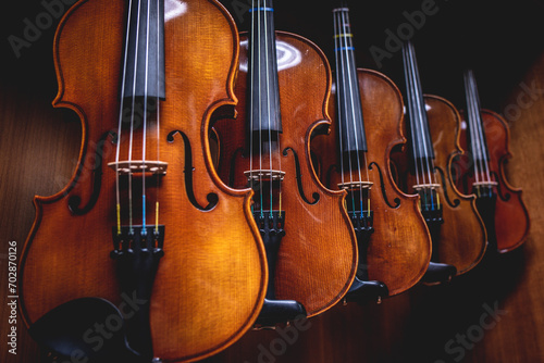 Row of multiple violins hanging on the wall, musician workshop