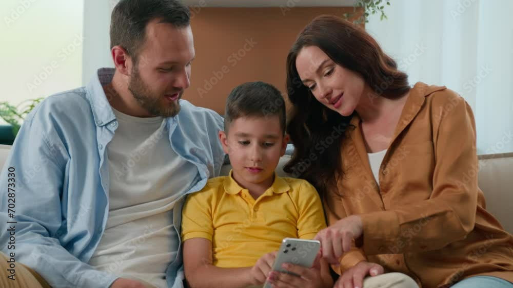 Happy family father mother parents son kid boy child talk communicate looking smartphone screen together on couch home using mobile app for play watch video on Internet browsing social media on phone Happy family father mother parents son kid boy child talk communicate looking smartphone screen together on couch home using mobile app for play watch video on Internet browsing social media on phone