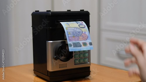 hand of a child lowering euro bills into the bill acceptor of a children's safe at home. European child saves money in a piggy bank safe. schoolchild's pocket money photo