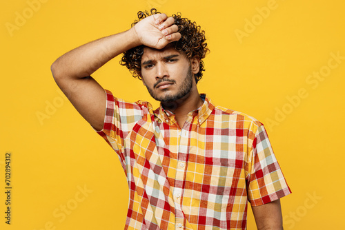 Young sick ill tired sad Indian man he wearing shirt casual clothes look camera put hand on forehead suffer from headache isolated on plain yellow color background studio portrait. Lifestyle concept.