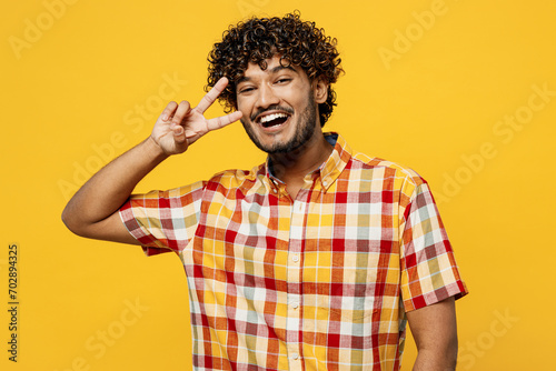 Young smiling happy cheerful satisfied Indian man wears shirt casual clothes show cover eye with victory sign look camera isolated on plain yellow color background studio portrait. Lifestyle concept.
