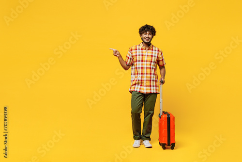 Traveler fun Indian man wear shirt casual clothes hold suitcase point aside isolated on plain yellow background. Tourist travel abroad in free spare time rest getaway. Air flight trip journey concept. #702894398