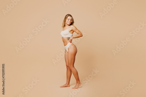 Full body side view young nice lady woman with slim body perfect skin wear nude top bra lingerie stand hold hands on waist panties isolated on plain pastel beige background Lifestyle diet fit concept