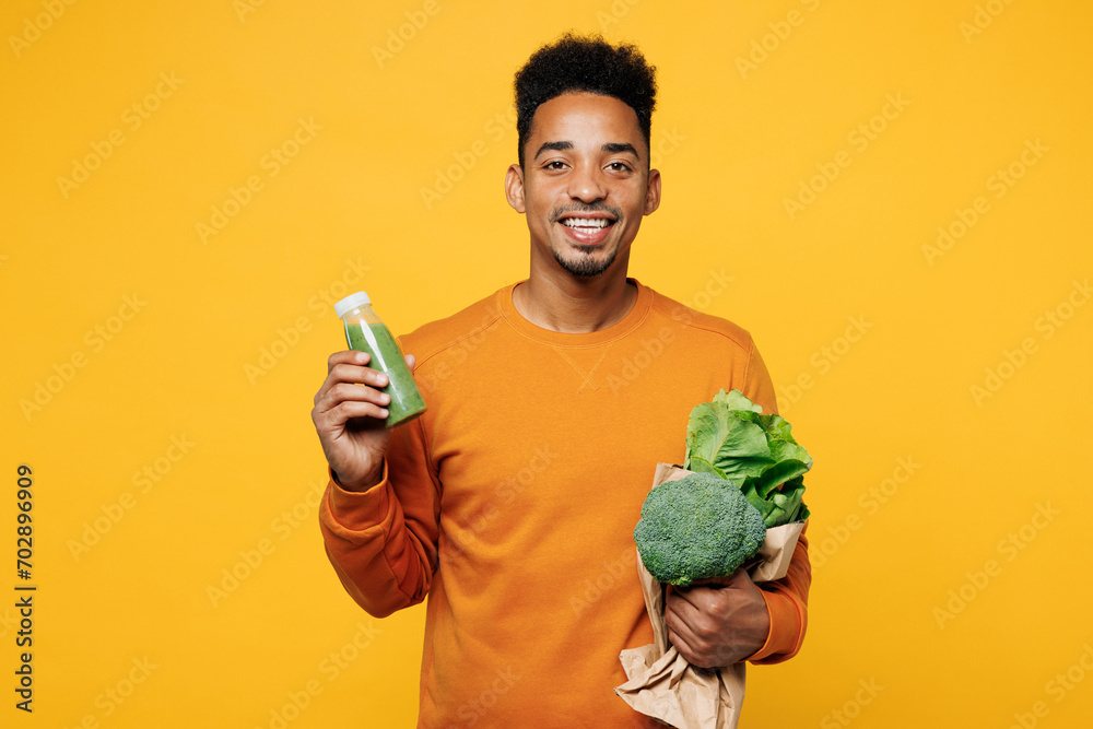 Young man wear casual clothes hold show juice green vegetable smoothie as detox diet, greenery herbs isolated on plain yellow background. Proper nutrition healthy fast food unhealthy choice concept.. Young man wear casual clothes hold show juice green vegetable smoothie as detox diet, greenery herbs isolated on plain yellow background. Proper nutrition healthy fast food unhealthy choice concept..