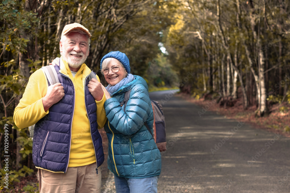 Happy senior couple enjoying nature outdoors in a mountain forest walking in the road. Joyful elderly couple with backpacks traveling together in Garajonay national park of La Gomera