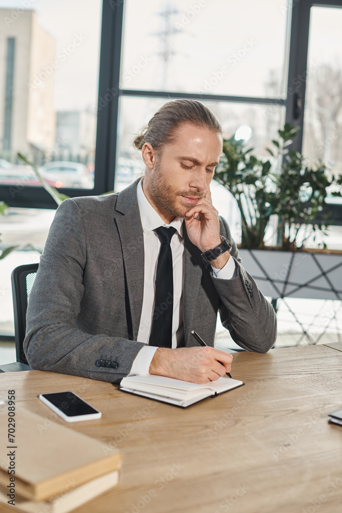 thoughtful businessman in formal wear writing in notebook near smartphone on work desk in office thoughtful businessman in formal wear writing in notebook near smartphone on work desk in office