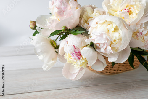 Light peonies in a wicker basket on a white wooden table © LariBat