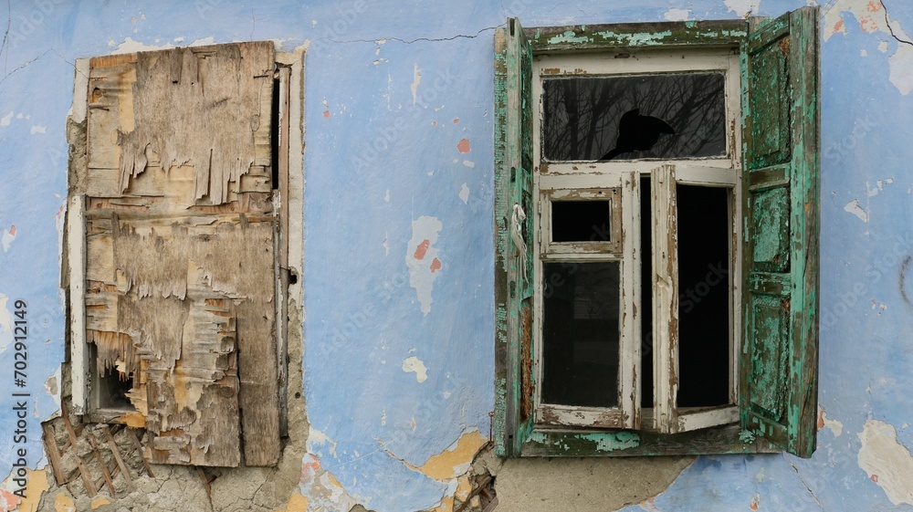 fragment of the facade of an old dilapidated building with one open glazed window and one window boarded up with plywood, the exterior of an old abandoned residential building