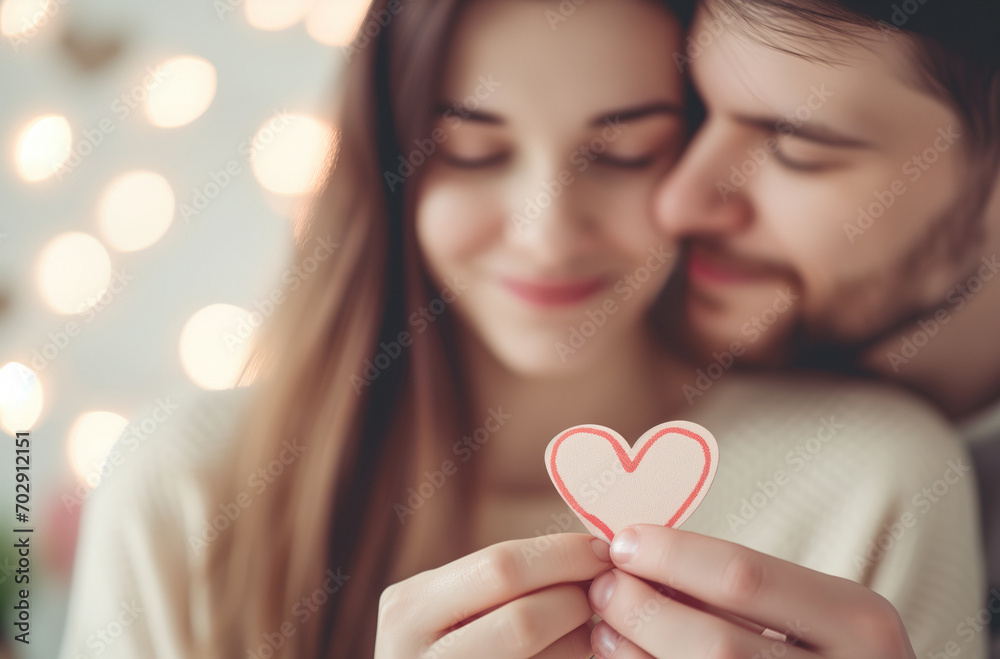 A moment of affection and fondness between a young couple in their home, holding a small cardboard heart in celebration of their prosperous future united by love, on Valentine’s Day