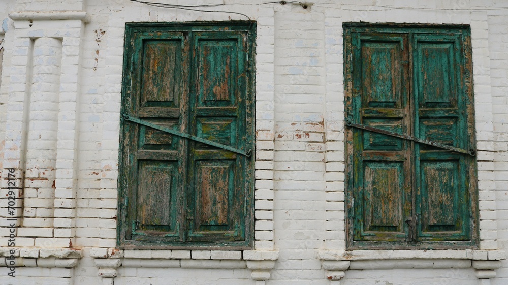 two windows of an old whitewashed house bolted with wooden shutters with peeling green paint, fragment of the exterior of an ancient building as a vintage background design, retro texture