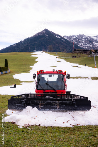 A snow groomer (snow cat, piste machine or trail groomer) waiting to be used to prepare the ski trails in the ski area in Walchsee, Tyrol, Austria. A ski piste and a ski lift (T-bar lift) in the back