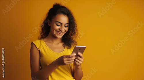 Easy payments. Happy young women make internet shopping use mobile phone and banking card purchase things online smile broadly dressed in casual t shirt isolated over vivid yellow background.