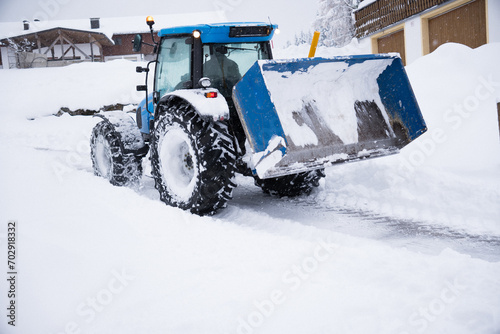 Onset of winter. Rear view of blue tractor with loader and snow chains clearing snow. Winter landscape