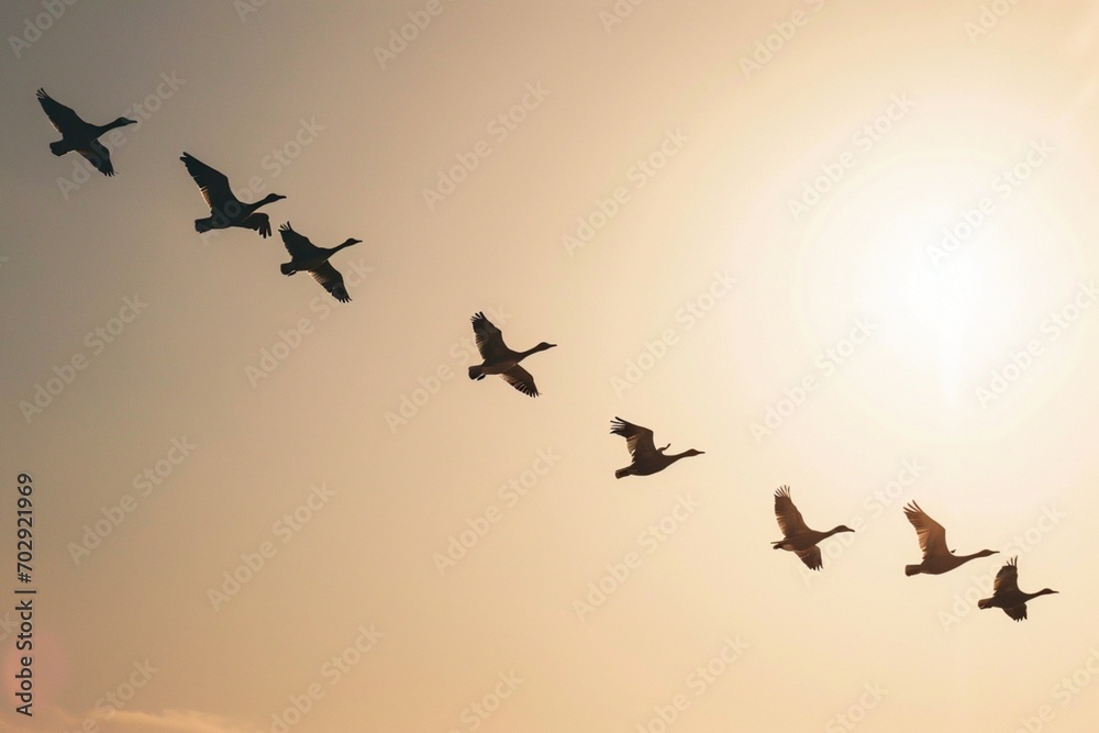 Fototapeta premium A flock of birds flying in a V-formation, symbolizing cooperation and collective effort, against a clear sky background.