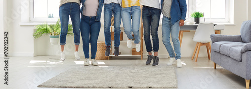 Happy friends having fun together. Group of young people in casual clothes jumping all together in a modern living room at home. Cropped shot, human legs, banner background photo