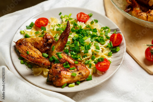 Farfalle pasta with grilled chicken wings on a white plate garnished with cherry tomatoes and green onions