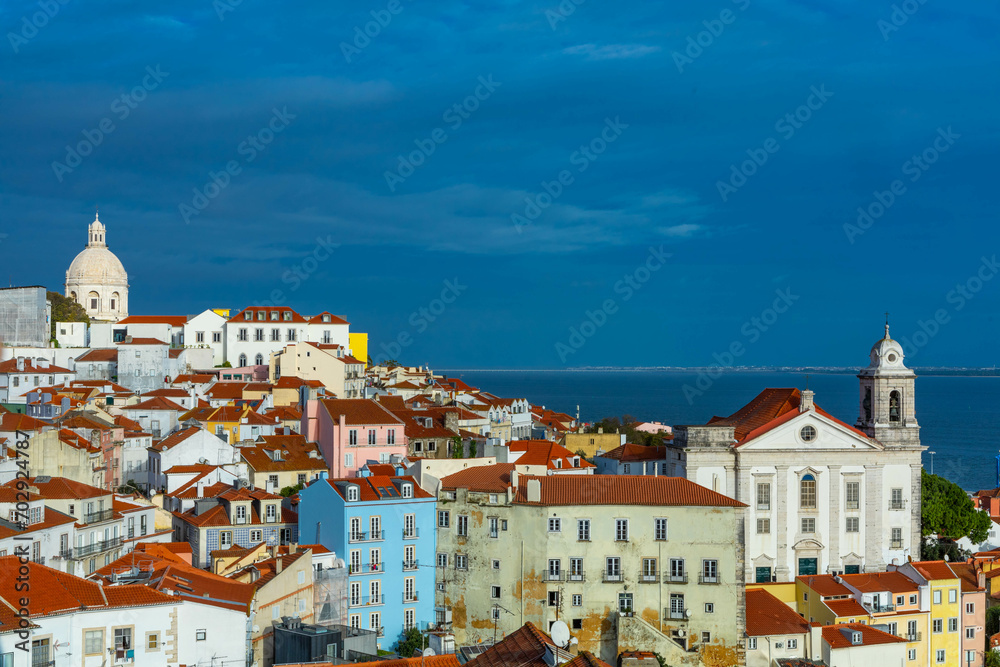 Lisbon, Portugal. 8 December 2023. Panoramic view of the beautiful skyline of Lisbon, Portugal, with orange roofed, colorful houses in the Alfama district during a sunny and cloudy day.