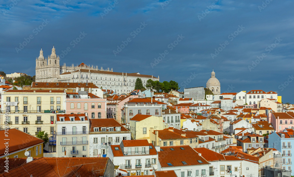 Lisbon, Portugal. 8 December 2023. Panoramic view of the beautiful skyline of Lisbon, Portugal, with orange roofed, colorful houses in the Alfama district during a sunny and cloudy day.