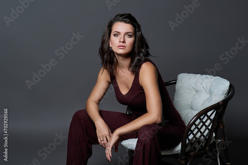 Fashionable young woman posing sitting in chair on dark gray studio background © Valerii Honcharuk