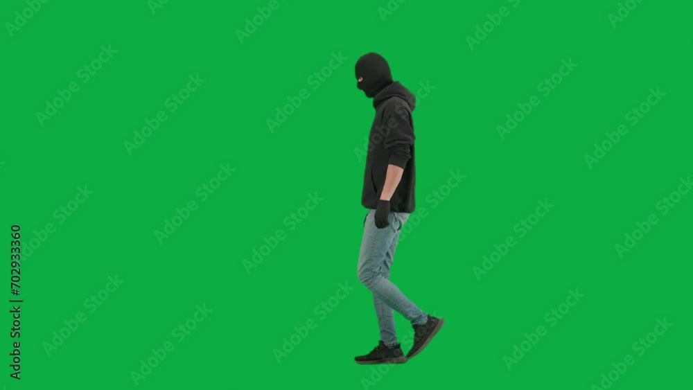 Portrait of thief on chroma key green screen background. Man robber wearing hoodie, jeans and black balaclava, walking getting ready for making a crime. Side view. Portrait of thief on chroma key green screen background. Man robber wearing hoodie, jeans and black balaclava, walking getting ready for making a crime. Side view.