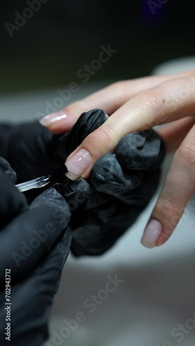 Manicurist applies transparent nail polish on woman's fingernail, detailed close-up. Professional manicure. Vertical video format.