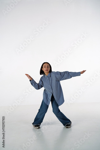 A young woman in denim casual wear poses in a studio against a white background. The dancer demonstrates the choreography elements of an experimental hip hop style dance. photo