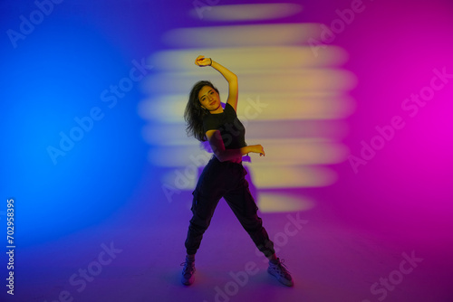 Photography Young woman in black clothes posing in studio with gradient blue, yellow, pink neon light