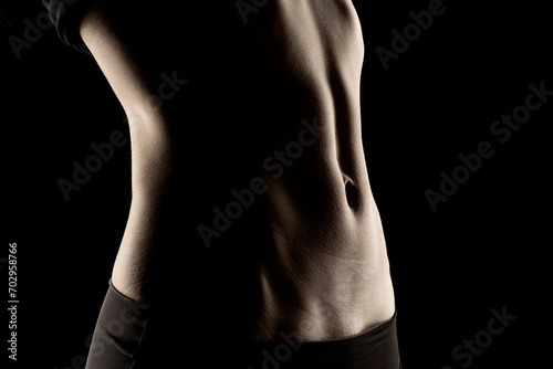 Close-up of a fit woman's stomach under the glow of light in a dark background photo
