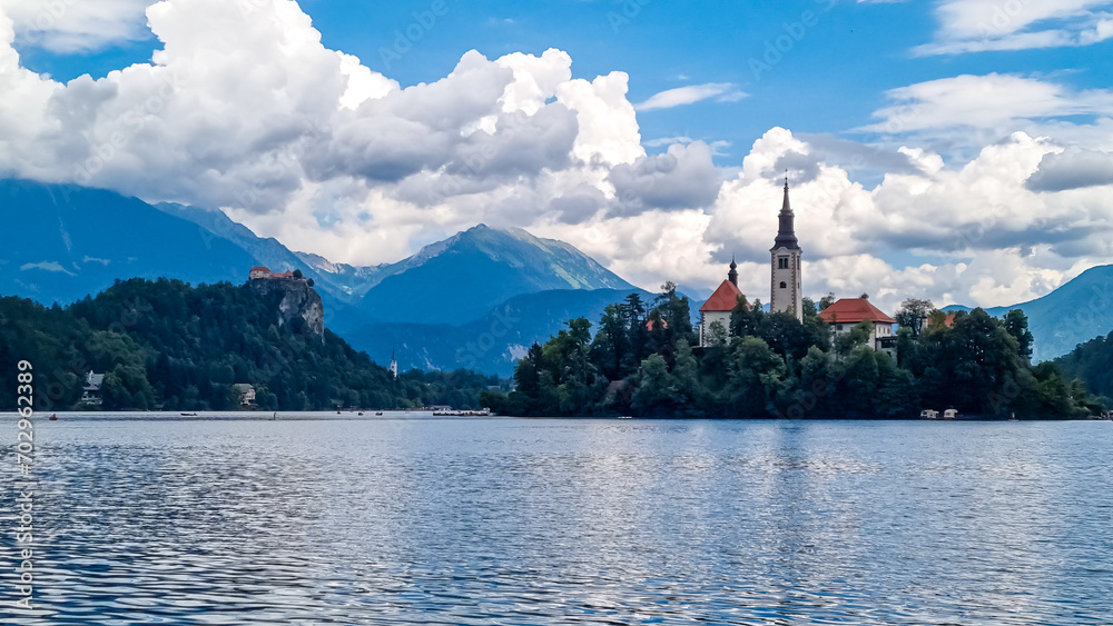 Panoramic view of St Mary Church of Assumption build on small island on alpine lake Bled, Upper Carniola, Slovenia. Serene landscape in Julian Alps in summer. Hills covered with lush green forest