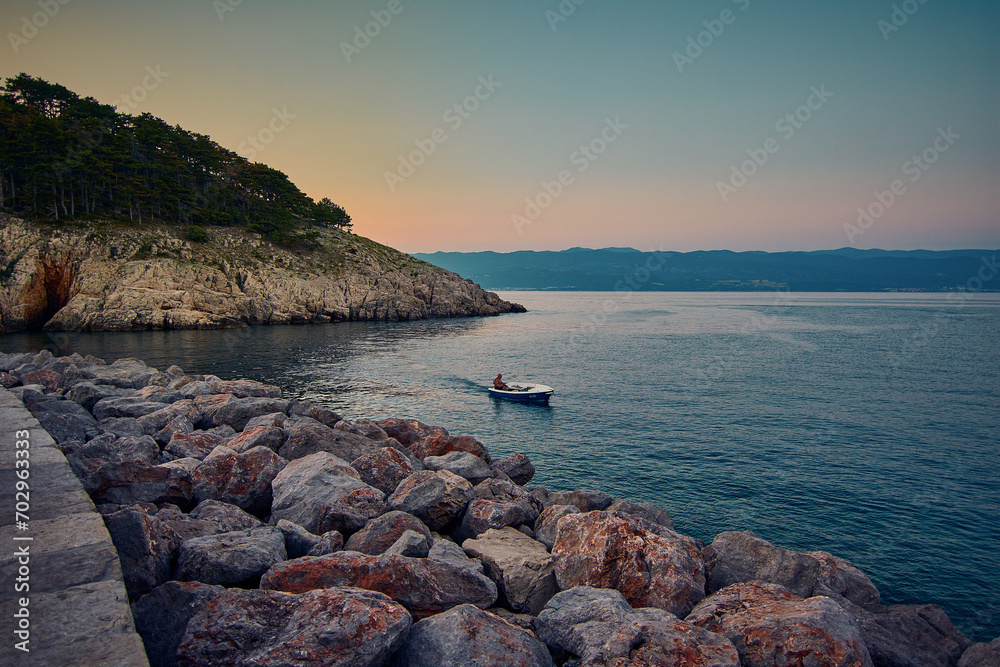 beautiful sunset over the sea with rocks and boat in the foreground