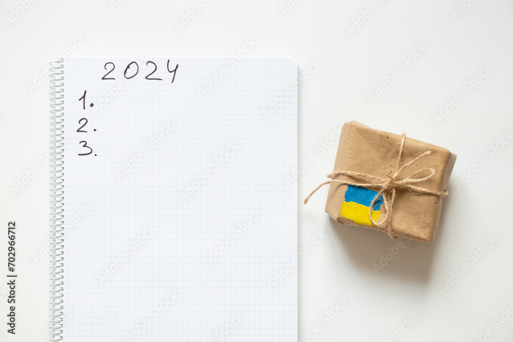 A notepad with the text 2024 and the number 123 and next to it there is a box with the flag of Ukraine on a white background, humanitarian aid for Ukraine A notepad with the text 2024 and the number 123 and next to it there is a box with the flag of Ukraine on a white background, humanitarian aid for Ukraine