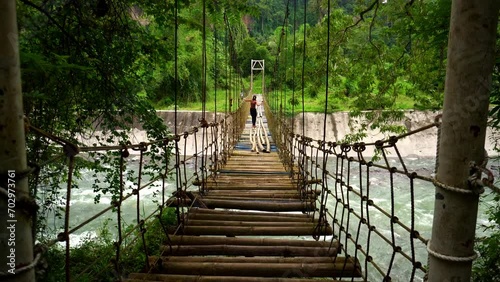 Long wobbly suspension bridge on ropes and cables made of bamboo over a strong mountain river with clear water in the tropics photo