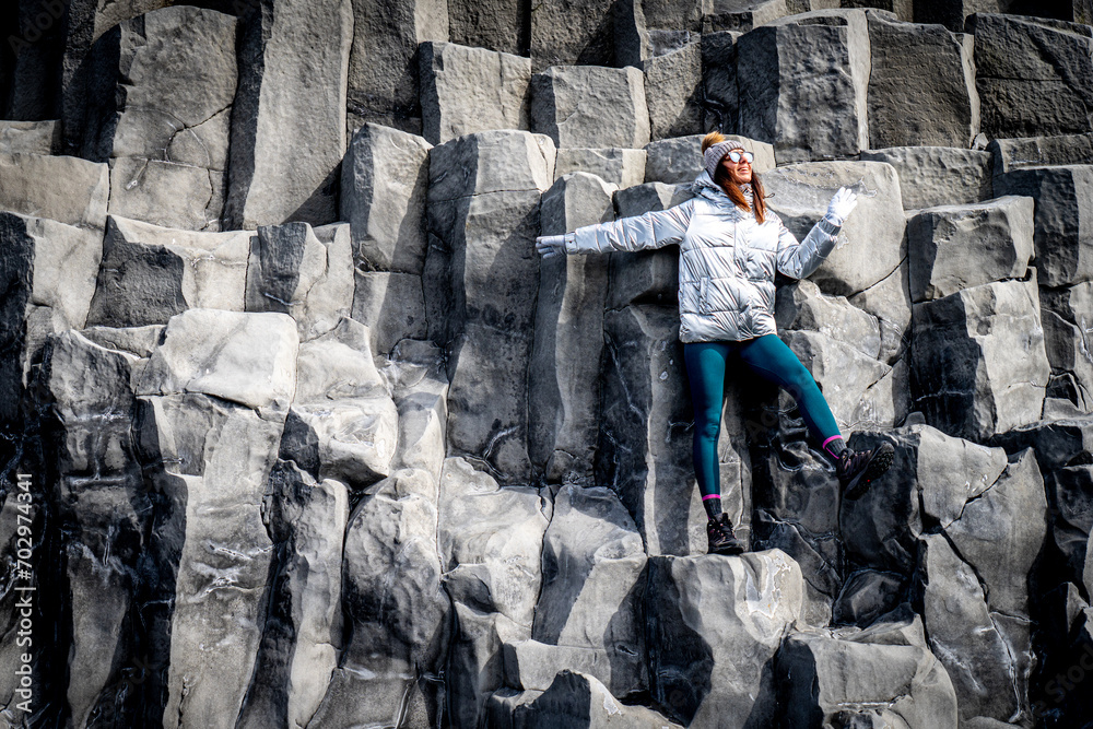 Woman in silver coat and beanie next to basalt formations in Reynisfjara, Iceland