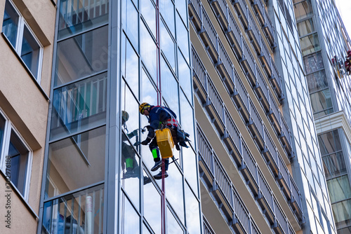 Bottom view of industrial mountaineering men in uniform washing glazing, hanging from building. Two males worker during high-rise job, rope access. Industry urban works concept. Copy ad text space