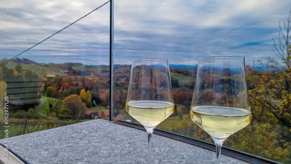 Obraz premium Drinking a glass of white wine with scenic view of vineyard during summer in Maribor wine region, Slovenia, Europe. Luxury couple get away vacation. Enjoying beverage in serene and romantic ambiance.