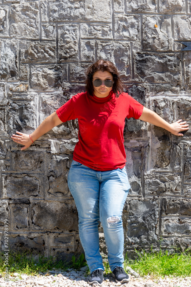 A girl in a red t-shirt and glasses stands against the wall with her arms spread out to the sides A girl in a red t-shirt and glasses stands against the wall with her arms spread out to the sides