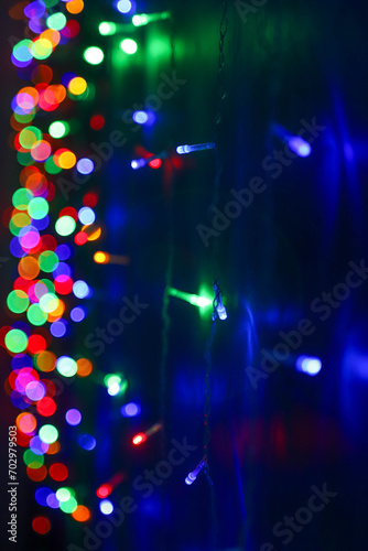 Strings of blue, red and green holiday lights in the dark as a background. Photo in perspective with selective focus