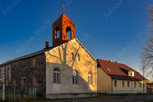 Der rostrote Glockenstuhl der denkmalgeschützte Dorfkirche Melchow am 66-Seen-Wanderweg leuchtet im Licht der Morgensonne