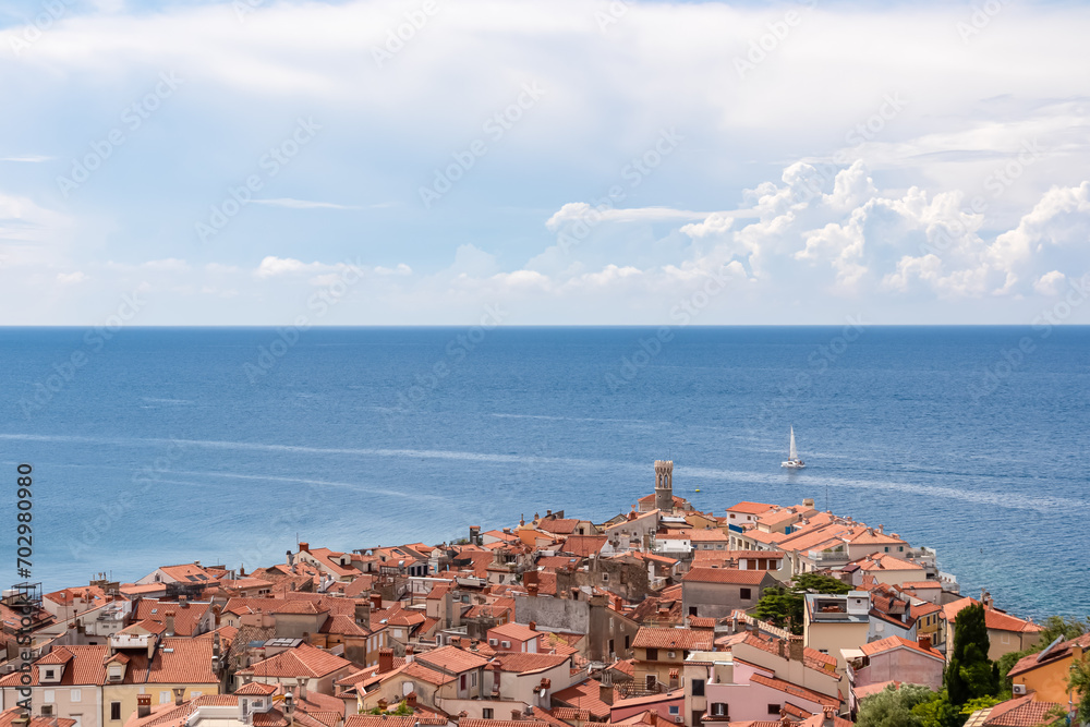 Small sailing boat at lighthouse of cape of coastal town of Piran, Primorska, Slovenia. Shimmering azure of Adriatic Sea. Tranquil Mediterranean atmosphere. Explore beauty at Slovenian Coast in Istria