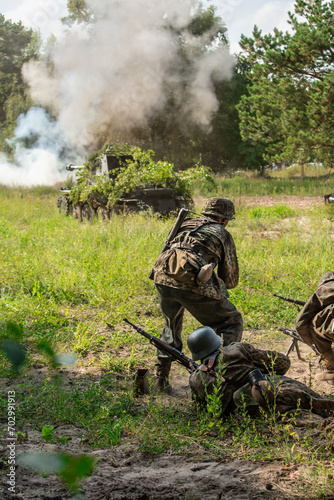 Historical reconstruction. German Wehrmacht Infantry soldiers from the World War II fight in the dust and smoke. View from the back.