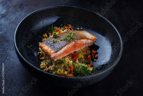 Traditional Mediterranean salmon fish fillet with vegetable cuscus served as close-up on a design bowl with copy space
